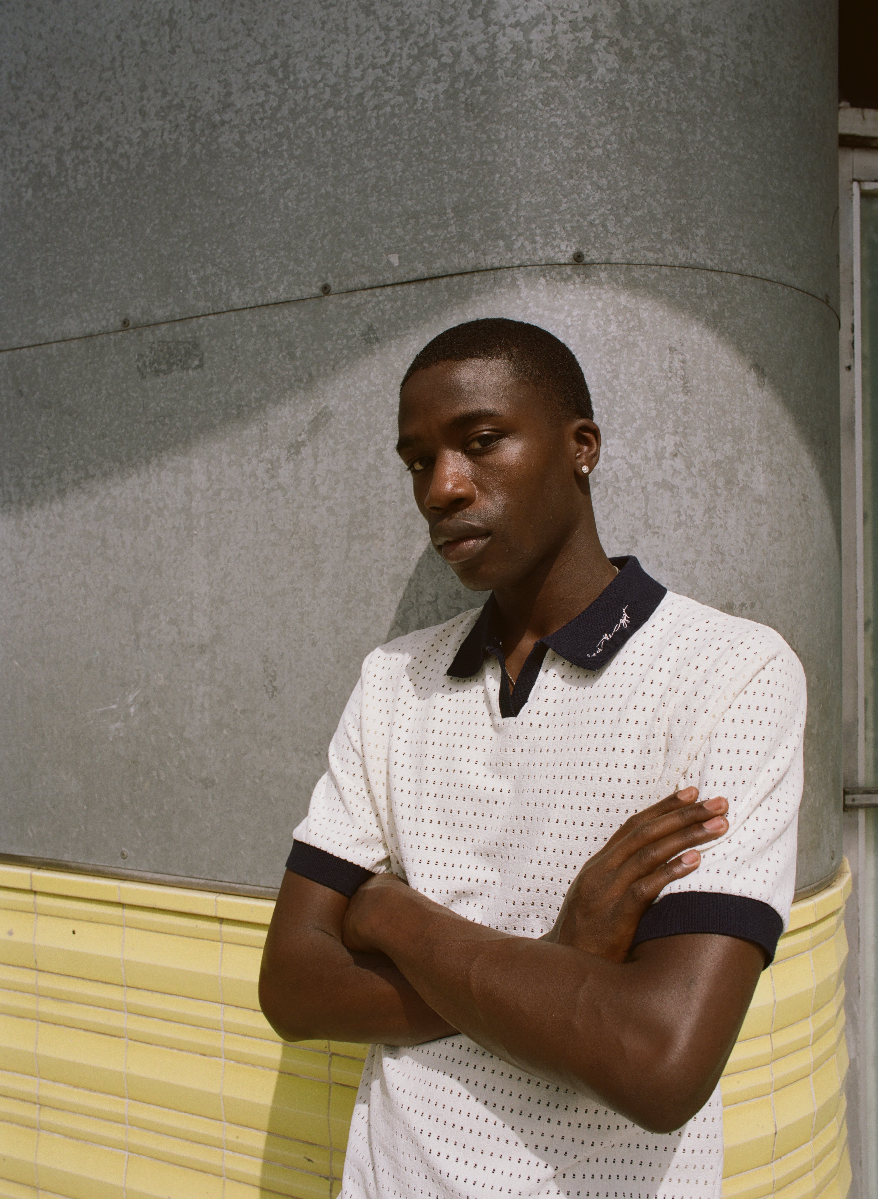 Man wearing a white textured shirt with black trim against a gray wall.