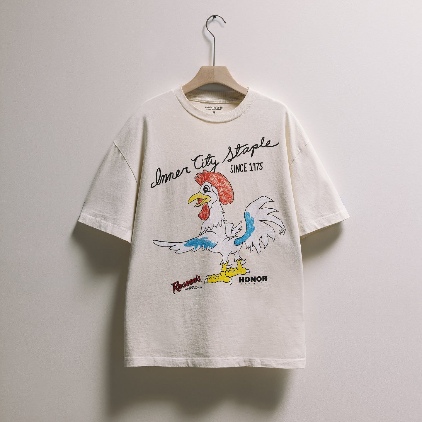 White t-shirt with a colorful rooster graphic and text on a white background